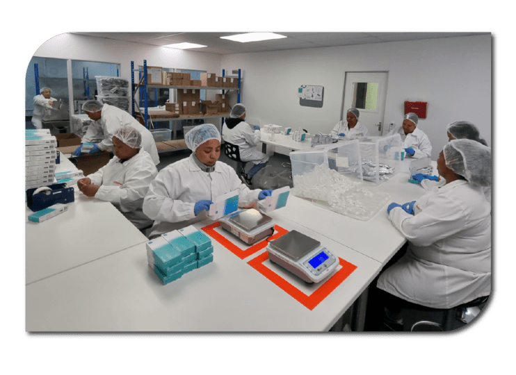 A diverse group of individuals in white lab coats collaborating on a manufacturing project.